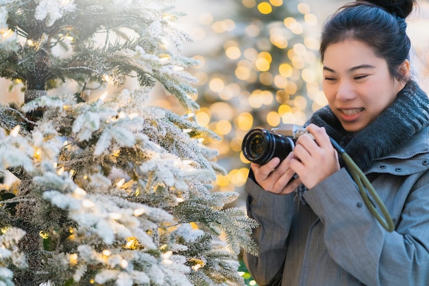 Geluk, mooie aziatische vrouwelijke handcamera, geniet van kerstboom met verlichting, versier en gouden wazige bokeh-achtergrond