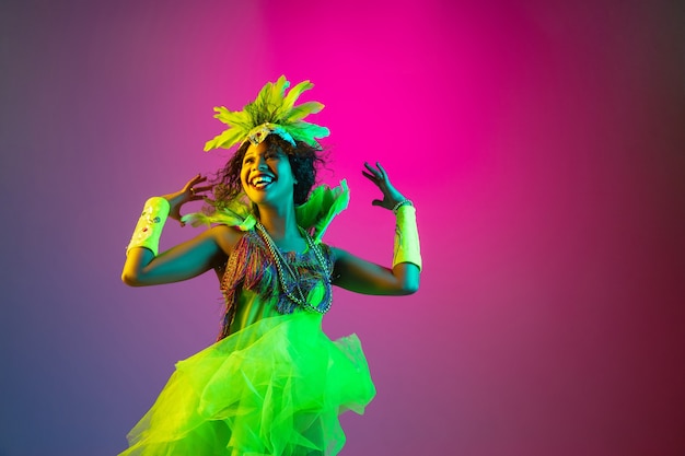 Geluk. Mooie jonge vrouw in Carnaval, stijlvol maskeradekostuum met veren die op gradiëntmuur dansen in neonlicht. Concept van vakantie, feestelijk, dans, feest, plezier maken.