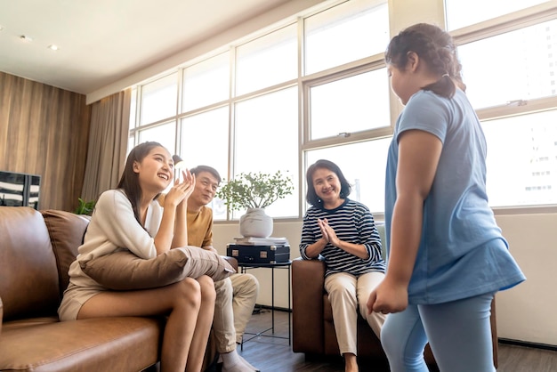 Geluk plezier aziatische mooie familie geniet van kijken en opvrolijken dochtertje meisje kind zang en dans oefenen voor tv in woonkamer thuis achtergrond