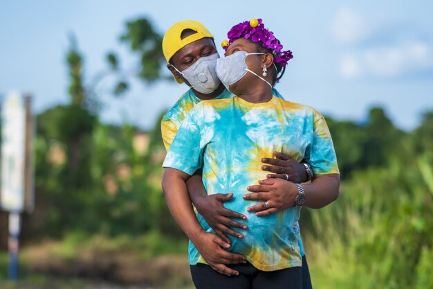 Gelukkig African American paar met een zwangere vrouw in beschermende gezichtsmaskers knuffelen en poseren