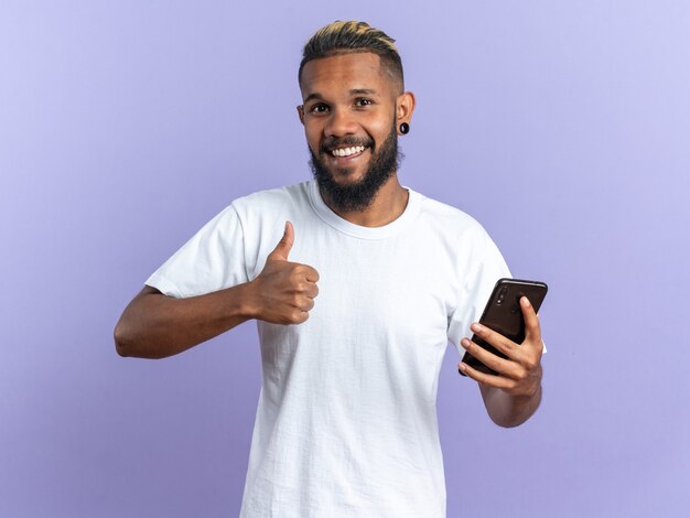 Gelukkig Afro-Amerikaanse jongeman in wit t-shirt met smartphone