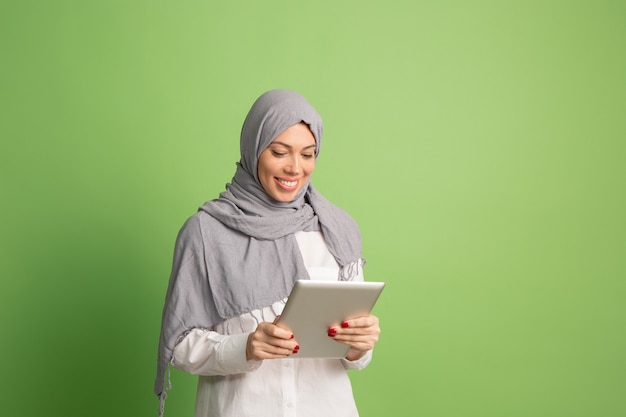 Gelukkig Arabische vrouw in hijab met laptop. Portret dat van glimlachend meisje, bij groene studio stelt.