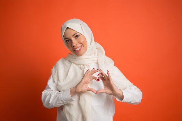 Gelukkig Arabische vrouw in hijab. Portret dat van glimlachend meisje, bij rode studioachtergrond stelt. Jonge emotionele vrouw. De menselijke emoties, gezichtsuitdrukking concept. Vooraanzicht.