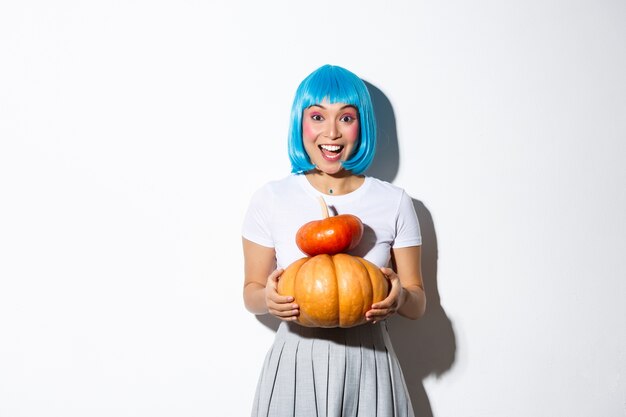 Gelukkig Aziatisch meisje in blauwe pruik met twee schattige pompoenen en glimlachend in de camera, schoolmeisje outfit dragen voor halloween-feest.