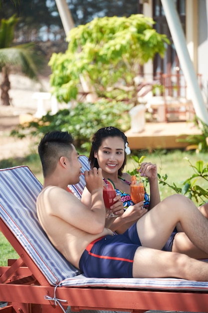 Gelukkig Aziatisch paar die van cocktails in openlucht op zonlanterfanters genieten