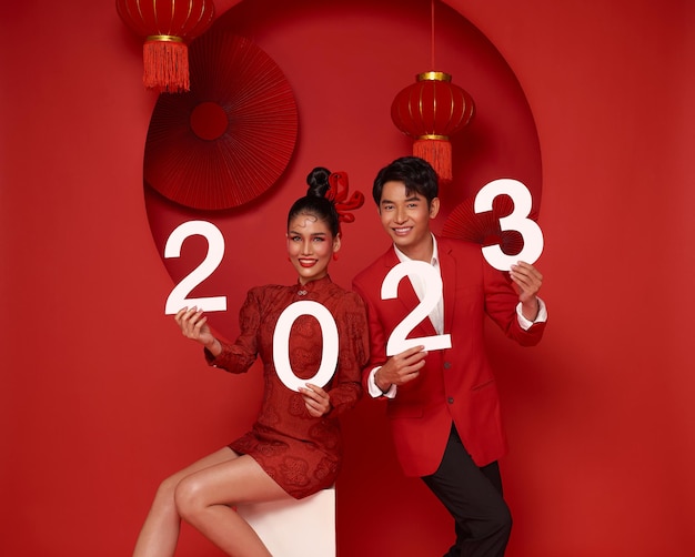 Gelukkig aziatisch paar in rode vrijetijdskleding met nummer 2023 en een gelukkig nieuwjaar begroet