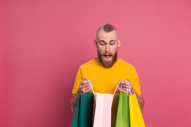 Gelukkig bebaarde positieve man casual look met kleurrijke boodschappentassen studio roze achtergrond