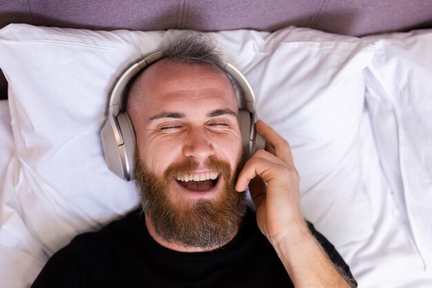 Gelukkig blanke man op bed met hoofdtelefoon luisteren genieten van zijn favoriete muziek, alleen rusten, dansen.