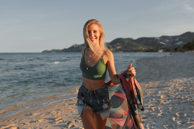 Gelukkig blond meisje dat op het strand loopt, dat van de zomer geniet.