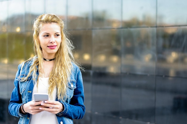 Gelukkig blonde jonge vrouw buiten met behulp van haar mobiele telefoon