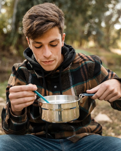 Gratis foto gelukkig camping man in het bos eten uit pot