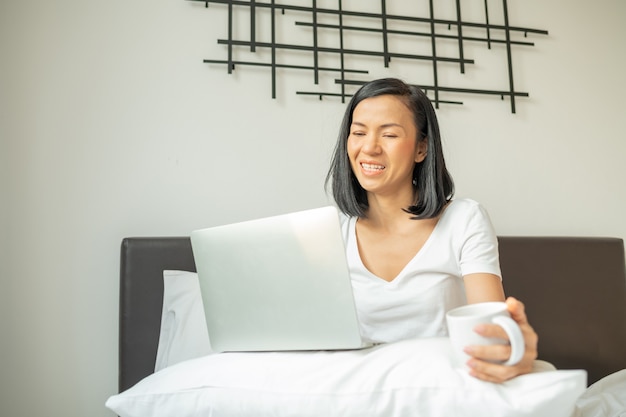 Gelukkig casual vrouw werkt op een laptop zittend op het bed in het huis.