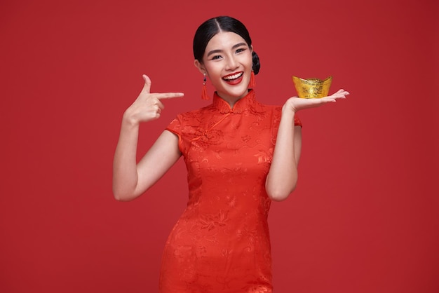 Gelukkig chinees nieuwjaar aziatische vrouw wijzend goudstaaf geïsoleerd op rode achtergrond
