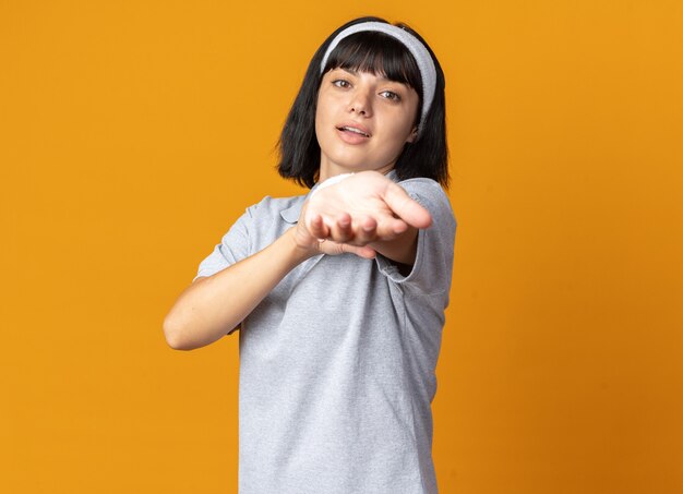 Gelukkig en zelfverzekerd jong fitnessmeisje met een hoofdband die haar handen uitrekt, klaar om te trainen en over oranje te staan
