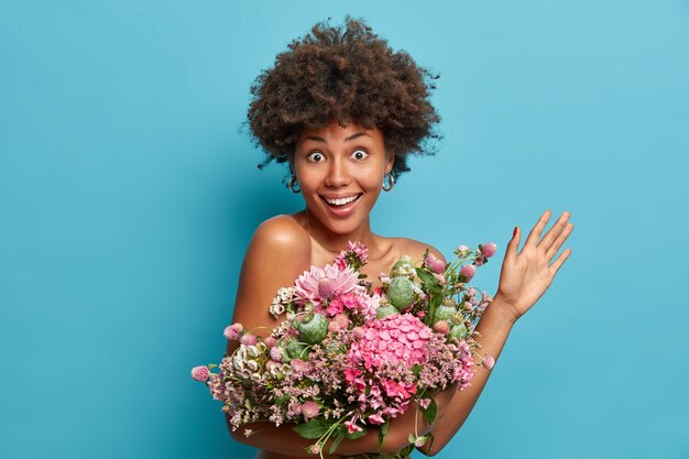 Gelukkig feest concept. Aantrekkelijke chique jonge dame houdt boeket bloemen verhoogt palm blikken met opgewonden vrolijke uitdrukking