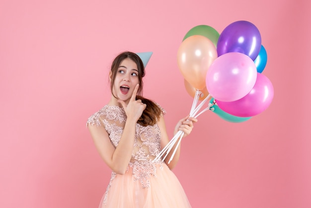 Gelukkig feestmeisje met feestmuts met ballonnen op roze