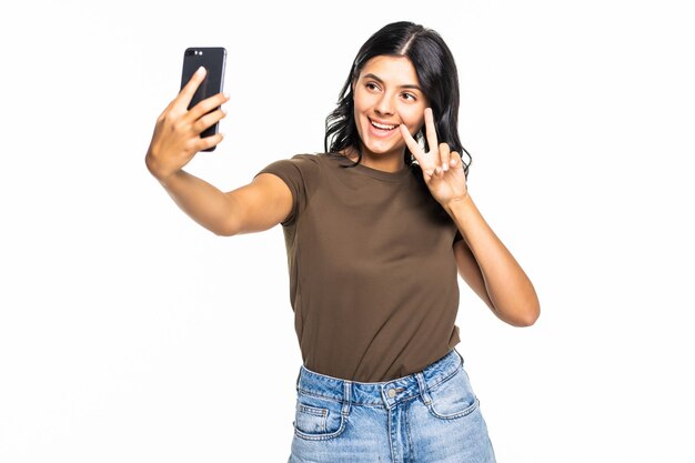 Gelukkig flirtend jong meisje dat foto's van zichzelf maakt op een smartphone, over een witte muur
