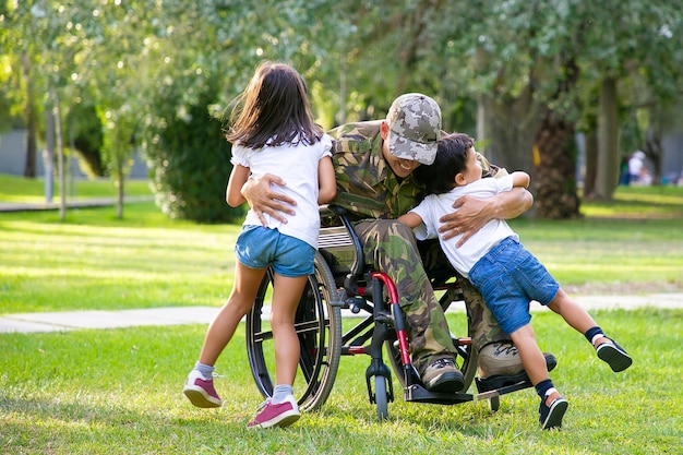 Gelukkig gehandicapte militaire man in rolstoel naar huis terugkeren en kinderen knuffelen. Veteraan van oorlog of gezinshereniging concept