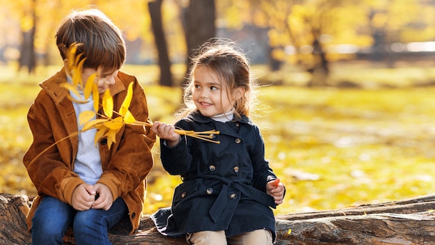 Gelukkig gezin in een herfstpark broer en zus zitten op een boomstam te spelen