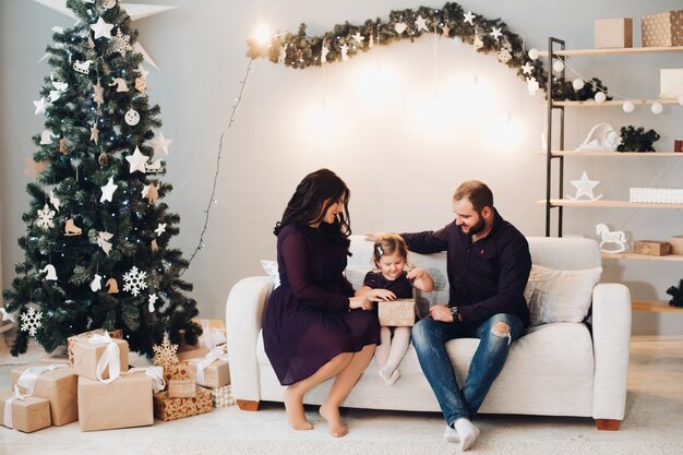 Gelukkig gezin met een kind zit op de bank naast de kerstboom en ontspant