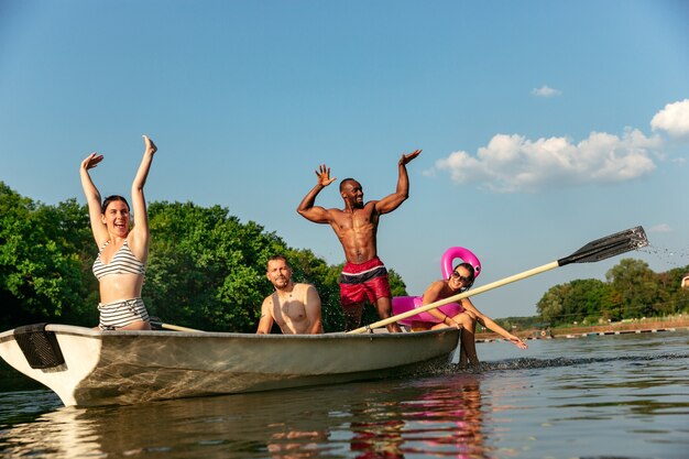 Gelukkig groep vrienden plezier tijdens het lachen en zwemmen in de rivier. Vrolijke mannen en vrouwen in zwembroek in een boot aan de rivier in zonnige dag. Zomer, vriendschap, toevlucht, weekendconcept.