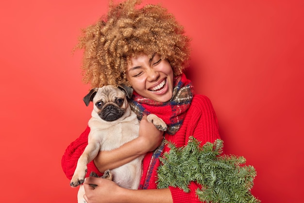 Gelukkig huisdier minnaar omhelzing met liefde pug hond drukt liefde en zorg uit heeft feestelijke stemming bereidt zich voor op kerstviering houdt groene krans gemaakt van dennenboom takken geïsoleerd op rode achtergrond