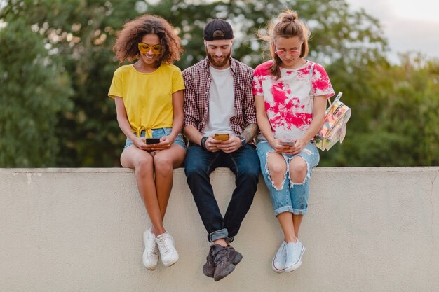 Gelukkig jong gezelschap van lachende vrienden zitten park met behulp van smartphones