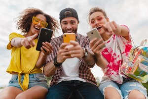 Gelukkig jong gezelschap van lachende vrienden zitten park met behulp van smartphones