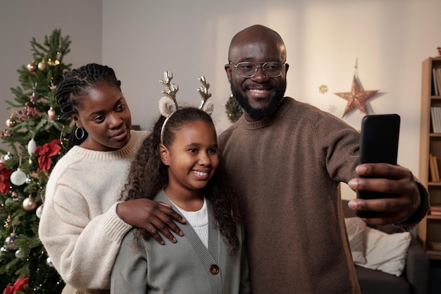 Gelukkig jong gezin van drie die selfie maken bij kerstboom