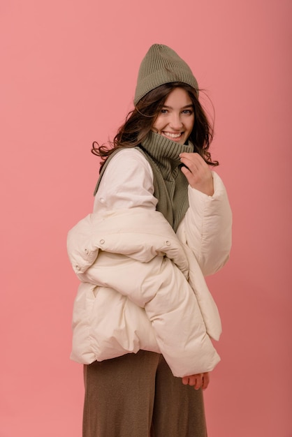 Gelukkig jong kaukasisch brunette meisje in winterkleren glimlachend in de camera op roze achtergrond Winkelen in het koude seizoen