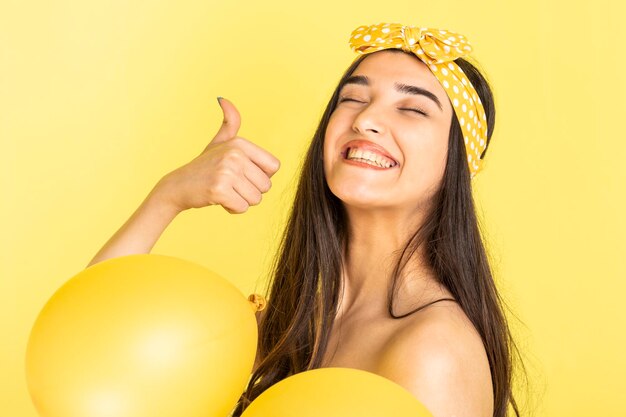 Gelukkig jong meisje met gele ballonnen en gebaar duim omhoog