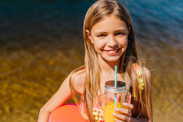 Gelukkig jong meisje met oranje drankje op strandvakantie