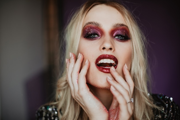 Gelukkig jong model met trendy make-up die goede emoties uitdrukt. Binnenfoto van bevallige blanke vrouw met blond golvend haar.