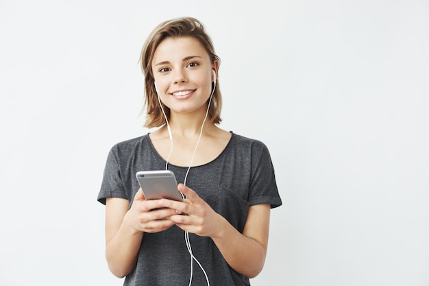 Gelukkig jong mooi meisje dat in hoofdtelefoons telefoon het glimlachen houdt.