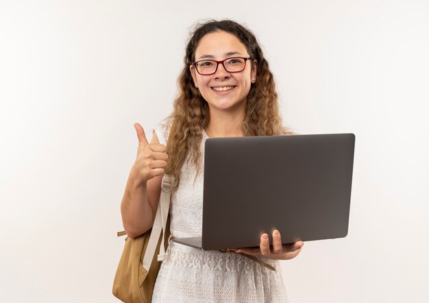 Gelukkig jong mooi schoolmeisje die glazen en laptop van de achterzakholding dragen die duim tonen die omhoog met exemplaarruimte wordt geïsoleerd