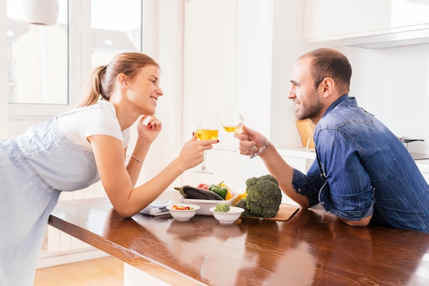 Gratis foto gelukkig jong paar dat de wijnglazen met verse salade op lijst roostert