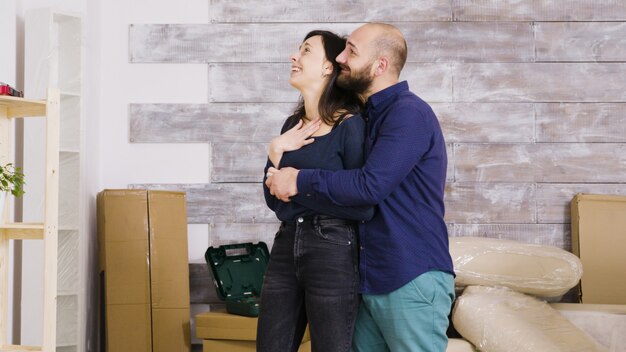 Gelukkig jong stel knuffelen elkaar in hun nieuwe appartement. Kartonnen dozen op de achtergrond.