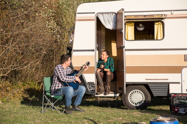 Gelukkig jong stel ontspannen in de bergen met hun retro camper. Vriendje speelt op gitaar voor zijn vriendin.