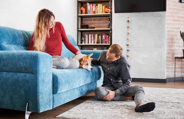 Gelukkig jong stel speelt thuis met schattige Corgi-hond