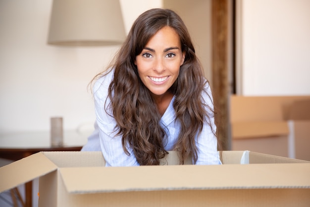 Gelukkig jonge Latijnse vrouw dingen uitpakken in haar nieuwe appartement, kartonnen doos openen,