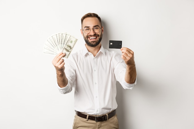 Gelukkig jonge man met zijn creditcard en geld dollars, glimlachend tevreden, permanent