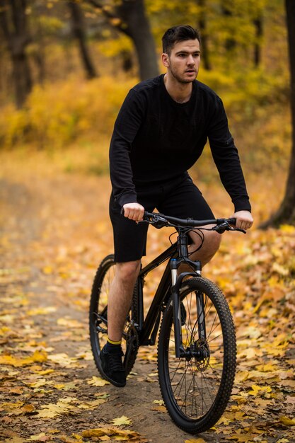 Gelukkig jonge man wielrenner rijdt in het zonnige bos op een mountainbike. Avonturen reis.