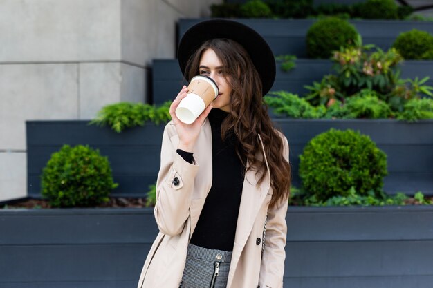 Gelukkig jonge trendy vrouw drinken afhaalmaaltijden koffie en wandelen na het winkelen in een stedelijke stad.