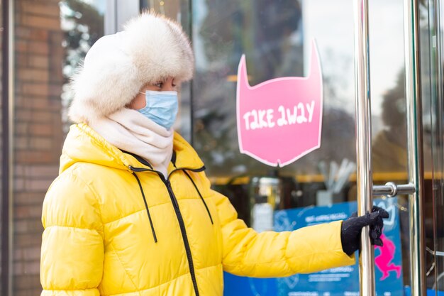 Gelukkig jonge vrouw aan de deur van het restaurant op een koude winterdag, belettering, afhaalmaaltijden.