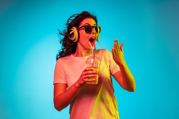 Gelukkig jonge vrouw dansen en glimlachen in koptelefoon over trendy blauwe neon studio