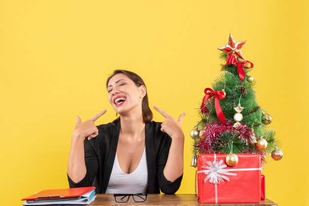 Gelukkig jonge vrouw in pak met versierde kerstboom op kantoor