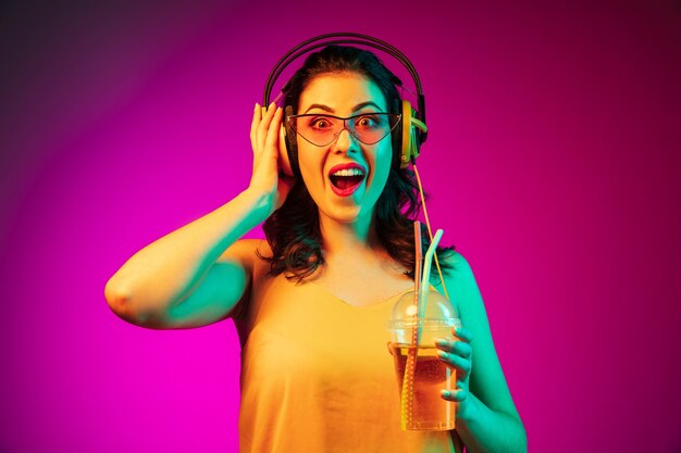 Gelukkig jonge vrouw in rode zonnebril drinken en luisteren naar muziek op trendy roze neon