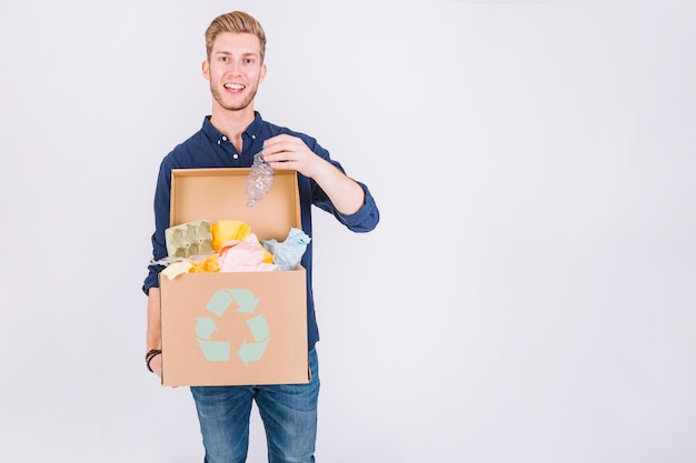 Gelukkig jongeman bedrijf kartonnen doos vol vuilnis met recycle pictogram