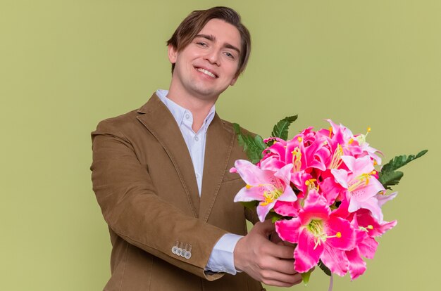 Gelukkig jongeman met boeket bloemen glimlachend vrolijk gaan feliciteren met internationale vrouwendag concept staande over groene muur