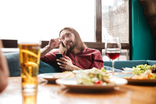 Gratis foto gelukkig jongeman zittend in café tijdens het gebruik van mobiele telefoon